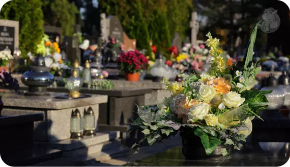 wiązanka sztucznych kwiatów ustawiona na pomniku zmarłego w otoczeniu zniczy